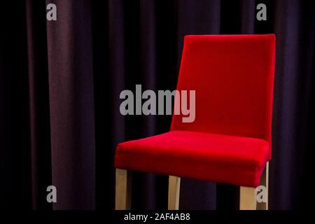 Ein roter Polsterstuhl neben lila Vorhänge. Stockfoto