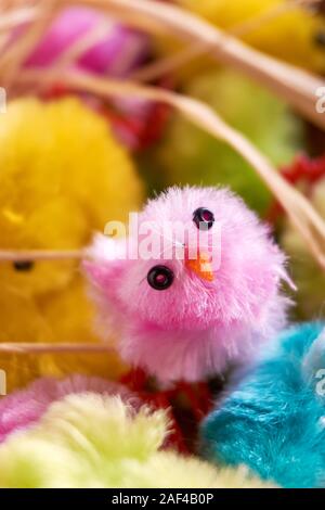 Flauschig Rosa, Gelb, Grün und Blau, kleinen fake Ostern Küken und natürlichen raffia Nistmaterial. Ein Huhn ist auf der Suche in die Kamera. Bild vertikal. Stockfoto