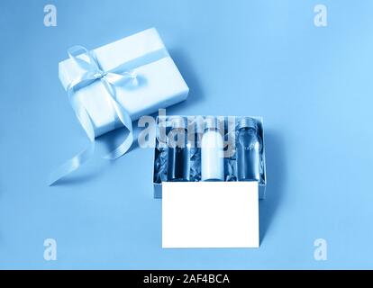 Geschenk Box mit drei kleinen mockup Flaschen Wellness kosmetische Produkte und leeren isoliert Label in trendigen Blau. Urlaub Geschenk Konzept. Mockup für Ihre Stockfoto