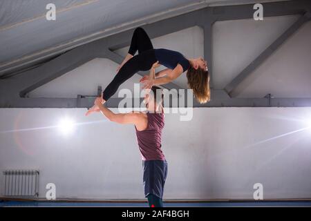 Das Thema der Acroyoga und Yoga Posen. Ein Paar aus zwei Männer und eine Frau stehen in der Position der Asana. Der Kerl hält das Mädchen gewölbt wieder hoch auf der Stockfoto