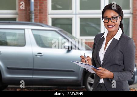 Afrikanische Frau mit Papieren über Zwischenablage mit Stift in der Nähe von geparkten Auto ausserhalb der Wohnung Stockfoto