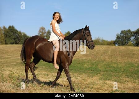 Happy teenage hübsches Mädchen auf Pony ohne Sattel auf Wiese in heissen Sommernachmittag Stockfoto