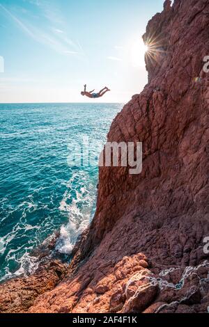 Junge männliche springt von rot sand Stone Cliff in Blue Ocean Stockfoto