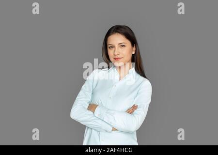 Freestyle. Junge Frau, die isoliert auf Grau verschränkte Arme lächelte zuversichtlich Stockfoto