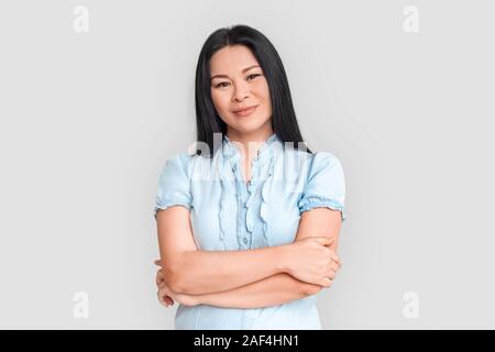 Freestyle. Asiatische Frau, die isoliert auf weißem verschränkte Arme lächelte zuversichtlich Stockfoto