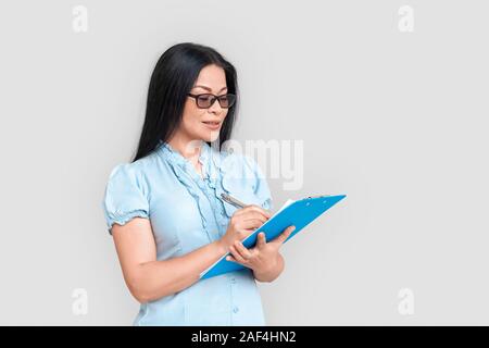 Freestyle. Asiatische Frau in Brillen isoliert auf weißem stehend mit Zwischenablage Notizen konzentriert Stockfoto