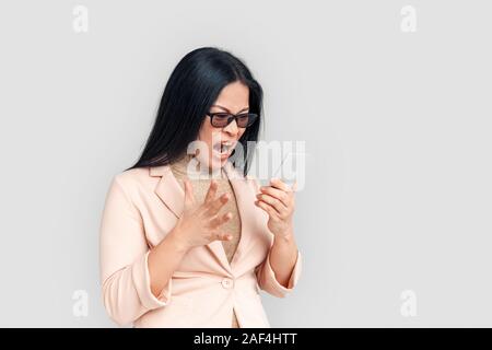 Freestyle. Asiatische Geschäftsfrau in Brillen isoliert auf weißem schrie Smartphone wütend stehend Stockfoto