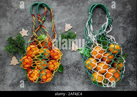 2 shopping Baumwolltasche mit Mandarinen und Weihnachtsbaum Niederlassungen auf grauem Beton Hintergrund. Weihnachten Null Abfall Konzept. Stockfoto