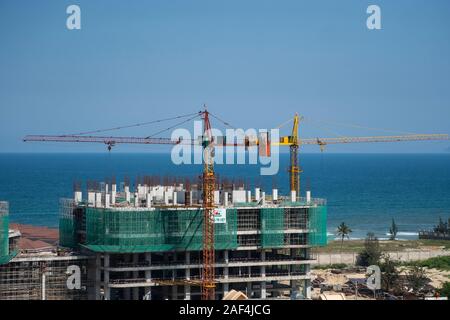 VIETNAM da NANG - April 10, 2019: Krane und Gebäude Baustelle gegen den blauen Himmel und das Meer. Metall Bau der unvollendete Gebäude auf Stockfoto