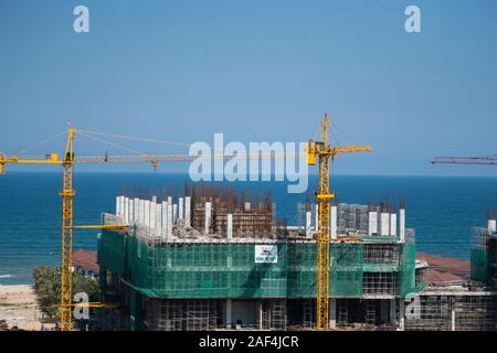 VIETNAM da NANG - April 10, 2019: Krane und Gebäude Baustelle gegen den blauen Himmel und das Meer. Metall Bau der unvollendete Gebäude auf Stockfoto