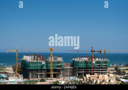 VIETNAM da NANG - April 10, 2019: Krane und Gebäude Baustelle gegen den blauen Himmel und das Meer. Metall Bau der unvollendete Gebäude auf Stockfoto