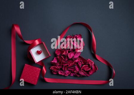 Rote Blütenblätter und Seidenband in der Form von Herzen und roter Geschenkbox auf schwarzem Hintergrund geprägt, herzlichen Glückwunsch Konzept Stockfoto