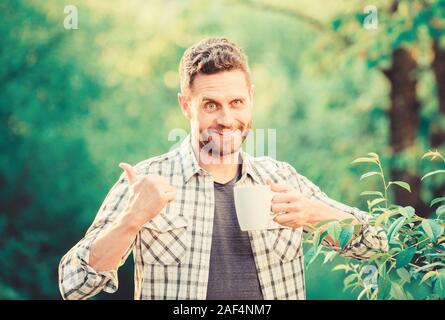 Gesunde Lebensweise. Ich bevorzuge grünen Tee. Erfrischendes Getränk. Man bärtige Kaffee Bauer halten Becher Natur Hintergrund. Grüner Tee Plantage. Vollständige blatt Tee. Angenehmen Moment der Self Care. Natürliche trinken. Stockfoto