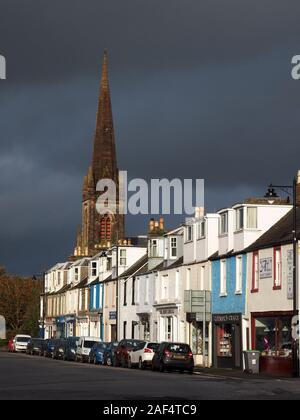 Kirchturm und weiß gestrichenen Gebäude Kontrast zum dunklen stürmischen Himmel im Hintergrund auf der Main Street in Kirkcudbright, Dumfries and Galloway, Schottland, Großbritannien Stockfoto