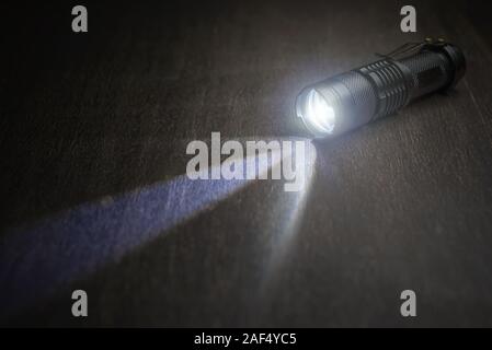 Taktische wasserdichte Taschenlampe. LED-Taschenlampe leuchtet auf dem Tisch in Rauch.. Stockfoto