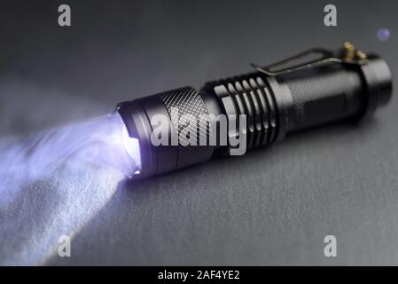 Taktische wasserdichte Taschenlampe. LED-Taschenlampe leuchtet auf dem Tisch in Rauch.. Stockfoto