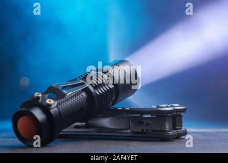 Taktische wasserdichte Taschenlampe. LED-Taschenlampe leuchtet auf dem Tisch in Rauch.. Stockfoto