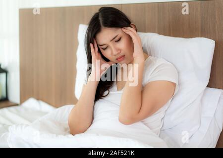 Attraktive junge asiatische Frau Aufwachen auf ihrem Bett ihre Hand von Kopfschmerzen und Suchen unglücklich und Gefühl Kopfschmerzen/Migräne/Stress/krank. Stockfoto