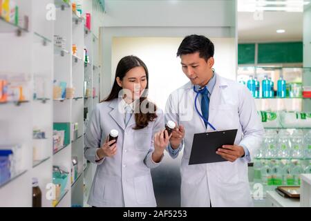 Zwei Asiatische junge Frau und Mann Apotheker mit einem reizenden Lächeln und Überprüfung bestand in der Apotheke und Drogerie. Medizin, Pharmazie, Gesundheit Stockfoto