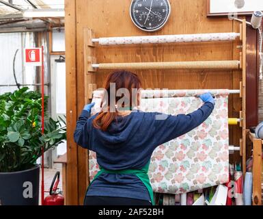 Junge Floristen mit roten Haaren arbeitet in einer Gärtnerei. Sie ist Schneiden Papier für das Paket. Gartenarbeit Konzept. Stockfoto