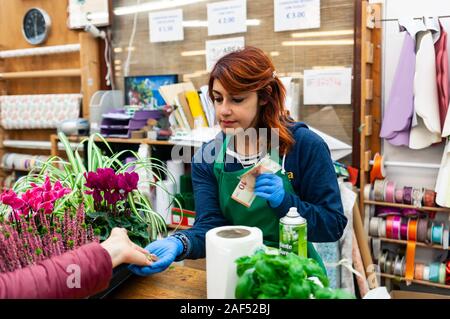 Junge Floristen mit roten Haaren arbeitet in einer Gärtnerei. Sie erhält Geld von einem Kunden zur Zahlung fällig. Stockfoto