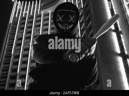 Porträt eines anonymen kriminellen Mann mit Baseballschläger in einer schwarzen Kapuze sein Gesicht hinter einer Maske. Helle Stadt Hintergrund Stockfoto