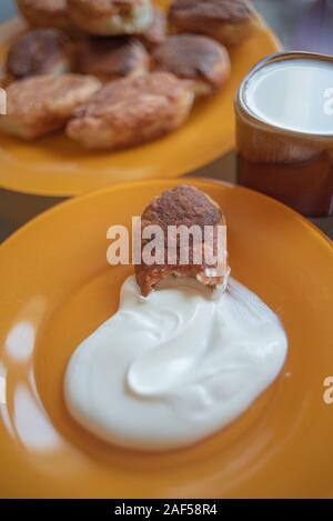 Teller mit gebratenen Torten. Saure Sahne Torte. Eine Torte in den Vordergrund und einen Teller mit Kuchen im Hintergrund. Tasse Milch und Kuchen gebraten auf gelbem Schild. Stockfoto