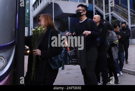 Dezember 12, 2019, Hongkong, China: Bürger mit einem Banner und Blumen Warteschlange auf einen Shuttlebus, der Sie in die Leichenhalle zu erhalten. Trauerfeier für spät Alex Chow (22.), ein Student Demonstrantin, die am 4. November dieses Jahres starb während eines Protestes wurde letzte Nacht statt. Chow's Tod, entsprechend "polizeiliche Untersuchung 'war' zertifiziert als "suicide warf sich vom Parkplatz auf dem Bürgersteig. Aber viele Bürger glauben, dass Alex Chow bin war urdered" durch die Polizei während eines Protestes, wenn er versuchte, aus der Szene der Konflikt auf die Straße zu entkommen, Stockfoto