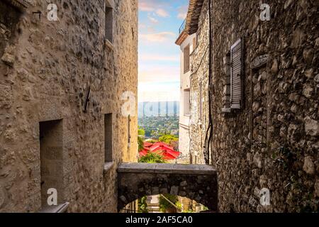 Die rote Schirme aus einem Cafe Terrasse und der Französischen Alpes-Maritimes Landschaft sind sichtbar von einer Gasse in mittelalterlichen Saint Paul de Vence, Frankreich Stockfoto