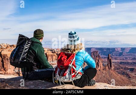 Ein Mann und eine Frau sitzen auf dem Rand des Canyon Wand den Blick über die schöne Landschaft des Canyonlands National Park und die La Sal Mountains, U Stockfoto