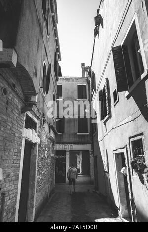 Touristen mit einem orange Rucksack und bandana Wanderungen entlang der schmalen Straße in Europa. Italien Venedig im Sommer. Die Fassade der alten Häuser ohne Menschen und Stockfoto