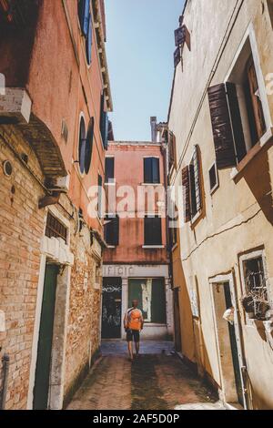 Touristen mit einem orange Rucksack und bandana Wanderungen entlang der schmalen Straße in Europa. Italien Venedig im Sommer. Die Fassade der alten Häuser ohne Menschen und Stockfoto