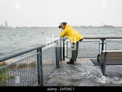 Ein Mann, der während des Hurrikans Sandy Fotos von der Sturmflut des East River gemacht hat, während das Wasser um ihn herum überflutete. Stockfoto