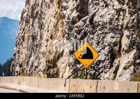 Watch für gefallene Rock und vorbereitet werden, um eine Kollision zu vermeiden. Warnung Verkehrszeichen auf Zement Barrieren, mit felsigen Abhang Hintergrund Stockfoto