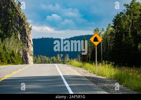 Watch für gefallene Rock und vorbereitet werden, um eine Kollision zu vermeiden. Mit einem felsigen Abhang auf der linken Straßenseite, Warn Schilder. Stockfoto