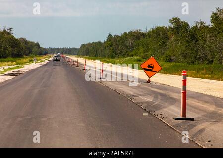 Straße im Bau mit neuen Asphalt, vorübergehender Zustand Zeichen, Orange Fässer auf der rechten Strassenseite, Kanadische ländliche Landstraßen Stockfoto