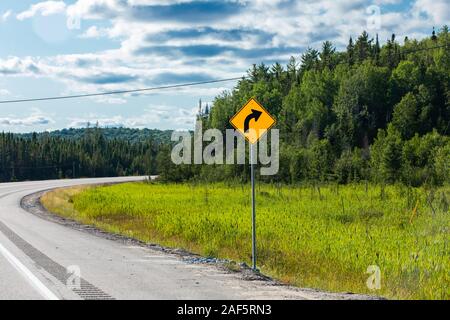 Leichte Biegung oder Kurve in der Straße vor, Warnung bei einer Kurve nach rechts, Warnung Schild am Straßenrand mit Pinien Wald Hintergrund Stockfoto