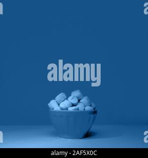 Schüssel mit riesigen Marshmallows auf soliden Hintergrund mit harten Schatten, getönt in Classic blau Stockfoto