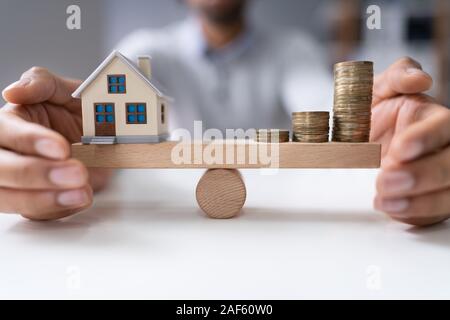 Der Unternehmer schützende Hand Balance zwischen Haus Modell und zunehmende Gestapelte Münzen auf Wippe Stockfoto