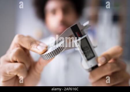 Close-up von der Größe eines Menschen Messgetriebe mit digitalen elektronischen Messschieber auf grauem Hintergrund Stockfoto