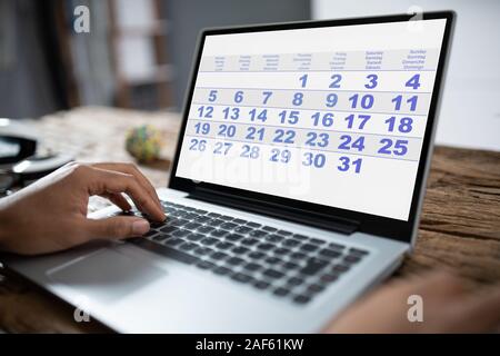 Junge Unternehmer auf der Suche nach Kalender auf Laptop am Schreibtisch Stockfoto