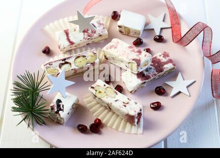 Nahaufnahme des Soft Nougat mit Beeren auf einem Teller mit Weihnachtsschmuck. Weißer Hintergrund Stockfoto