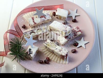 Nahaufnahme des Soft Nougat mit Beeren auf einem Teller mit Weihnachtsschmuck. Weißer Hintergrund Stockfoto