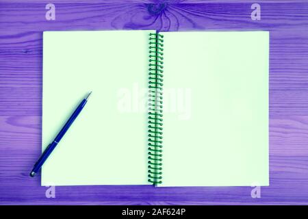 Leere Seite eines geöffneten Notebook mit einem blauen Stift auf lila Holztisch Stockfoto
