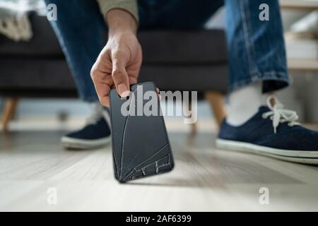 Nahaufnahme eines Mannes, der Kommissionierung, die Gebrochenen Smart Phone aus Hartholz Stock Stockfoto