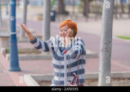 Lächelnd asiatische Frau Gespräche auf Ihrem Handy beim Anheben eine Hand. Unscharf Hintergrund. Stockfoto