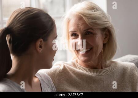 Lächelnde ältere Mutter und erwachsene Tochter zu Hause chatten Stockfoto