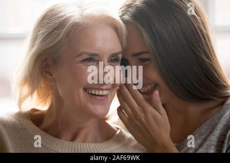 Lächelnd erwachsene Tochter teilen Geheimnis mit Happy senior Mom Stockfoto
