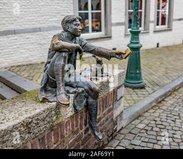 Seitenansicht eines Metall Statue eines Jungen, die ein Buch während des Sitzens auf die Wand in einer ruhigen Straße Stockfoto