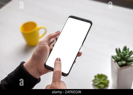Modernes Mobiltelefon mockup ih Frau Hände. Isoliert, mit einem leeren Bildschirm für App oder Website Design Promotion. Tasse Kaffee und Pflanzen auf den Schreibtisch im Hintergrund Stockfoto